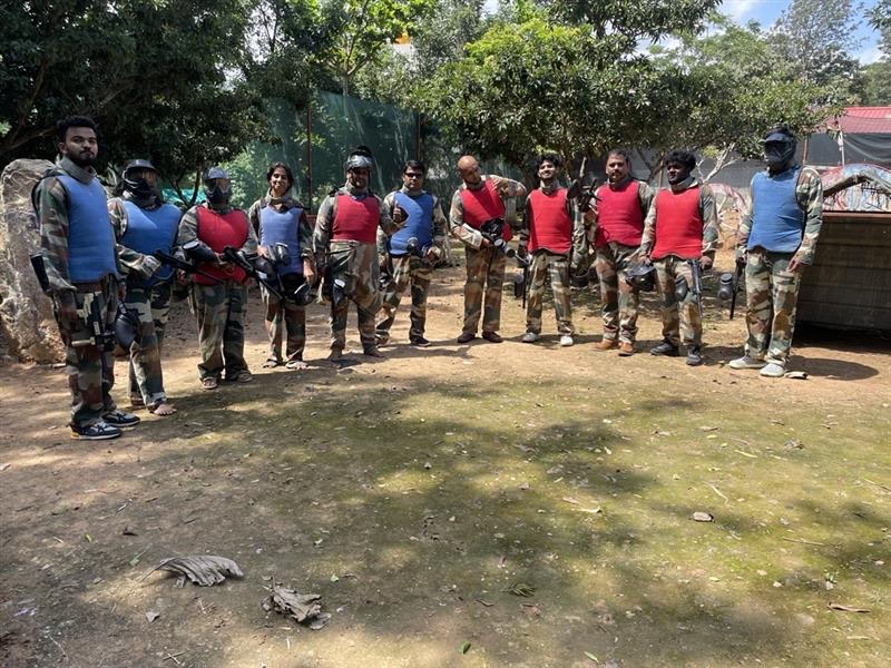 Colleagues lined up in paintball vests and helmets holding markers on a dirt field