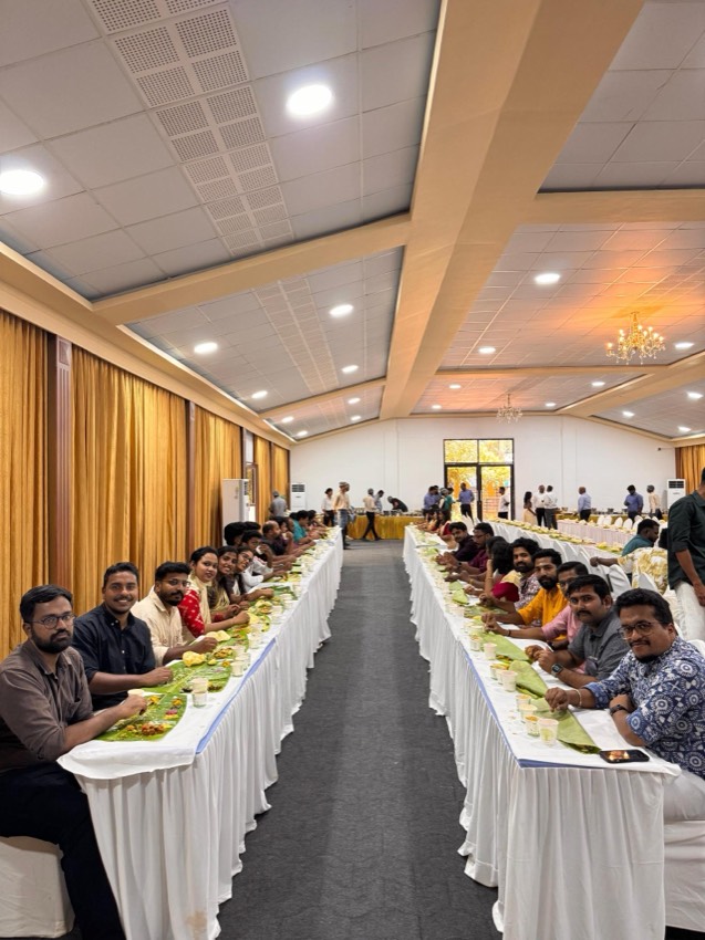 Two long banquet tables set for an Onam sadhya, with colleagues seated down both sides