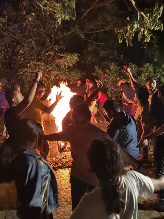 Colleagues gathered around a large bonfire at night with their arms raised