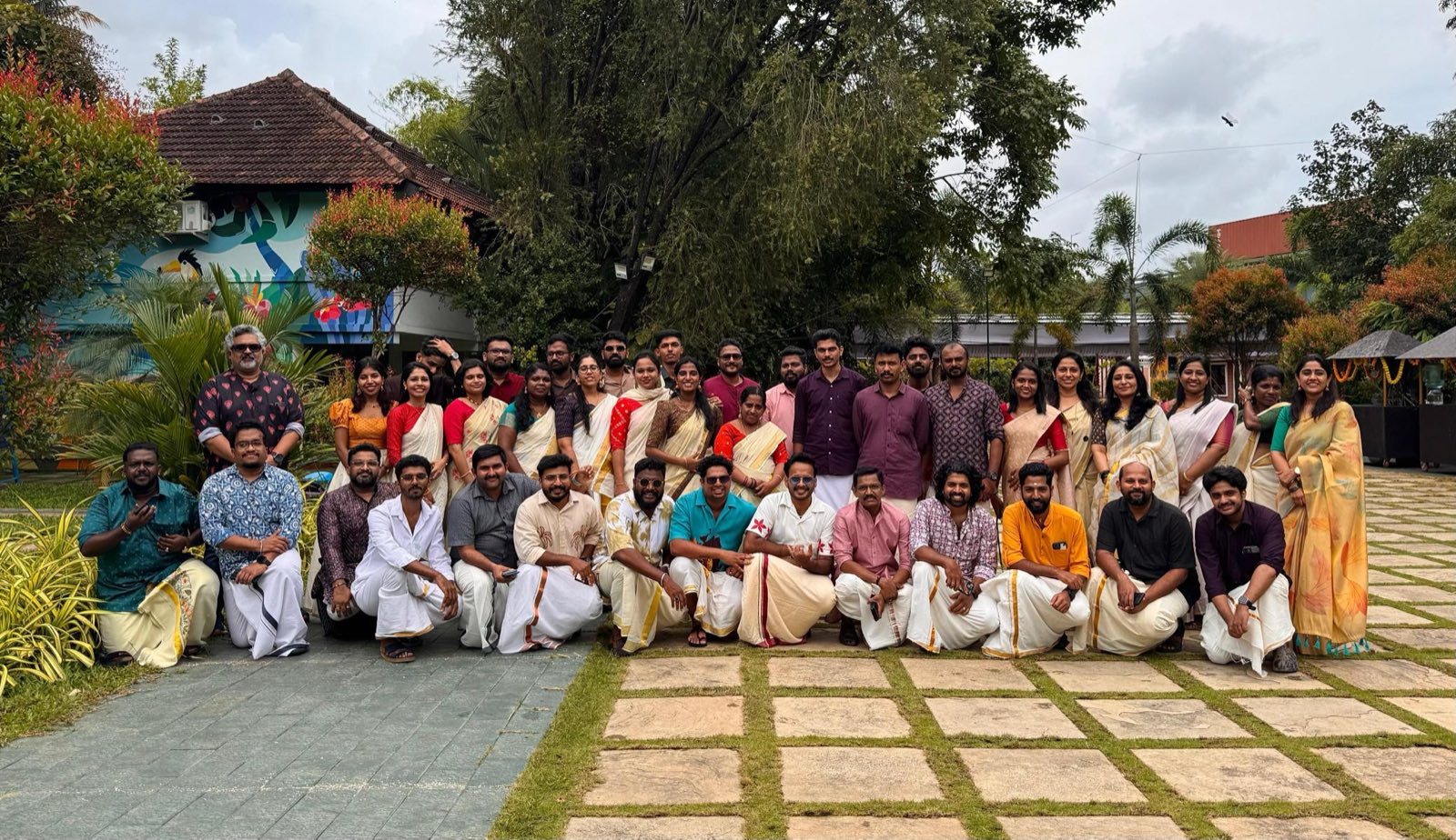 A large group of colleagues in Kerala traditional dress posing outdoors for an Onam group photograph