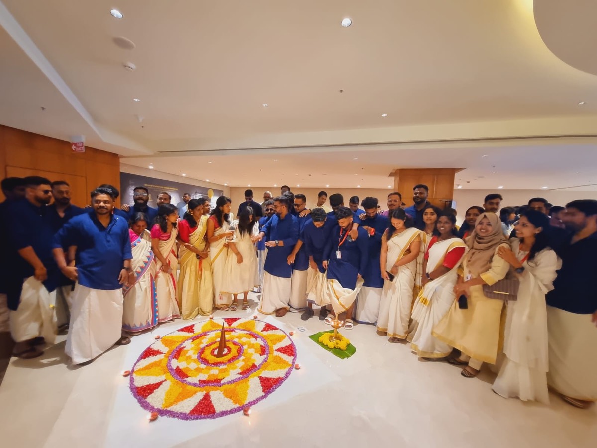 Colleagues standing in a semicircle around a circular flower pookalam laid on the floor