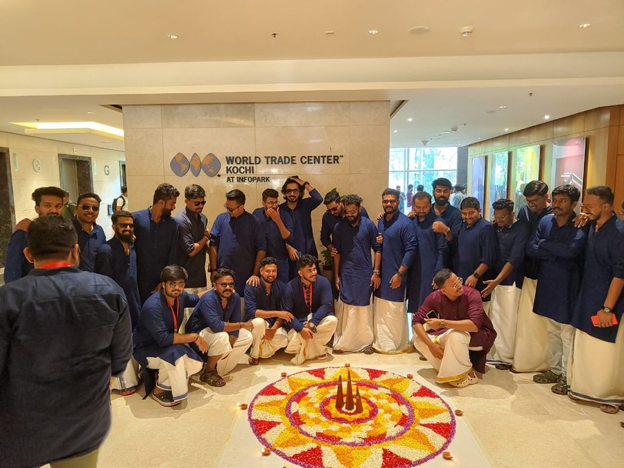 The team gathered around a pookalam in the World Trade Center Kochi lobby, with the building signage visible behind them