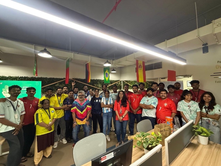 The team posing together in an assortment of national football jerseys between the office desks