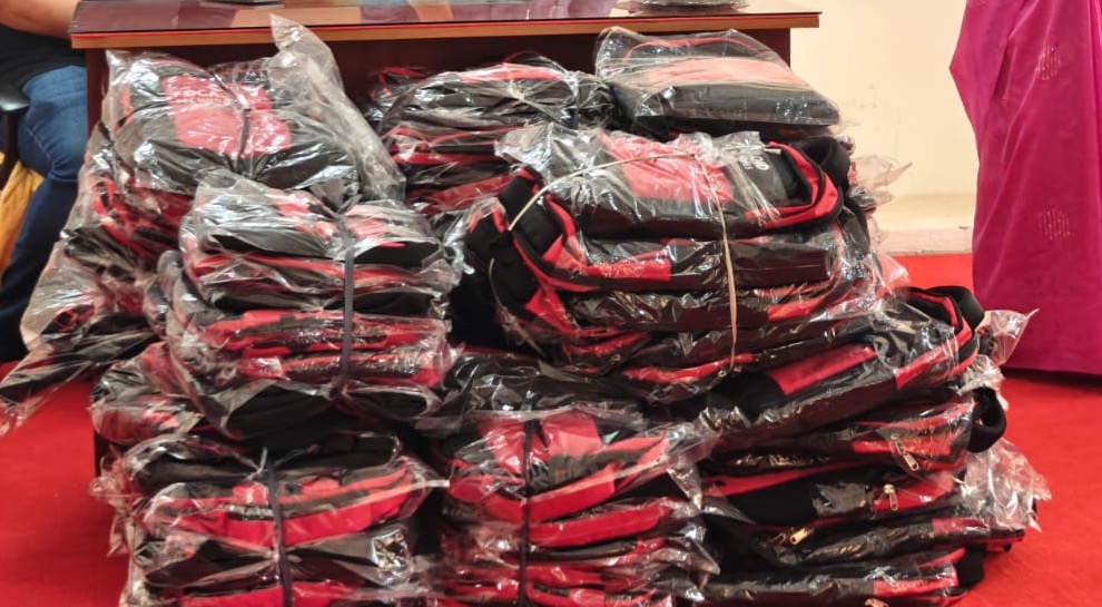 A large stack of individually packaged red and black Focaloid backpacks piled on the red carpet of a school hall
