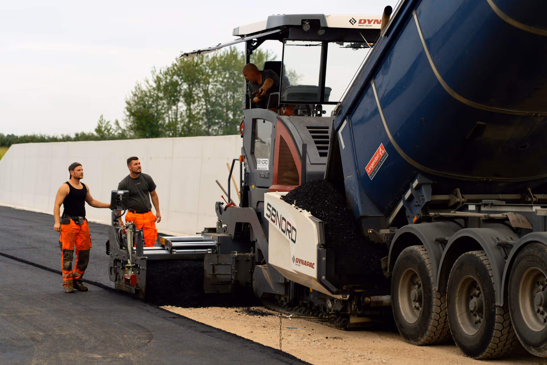 Drei Bauarbeiter verlegen Asphalt mit einer Dynapac Straßenfertigmaschine.