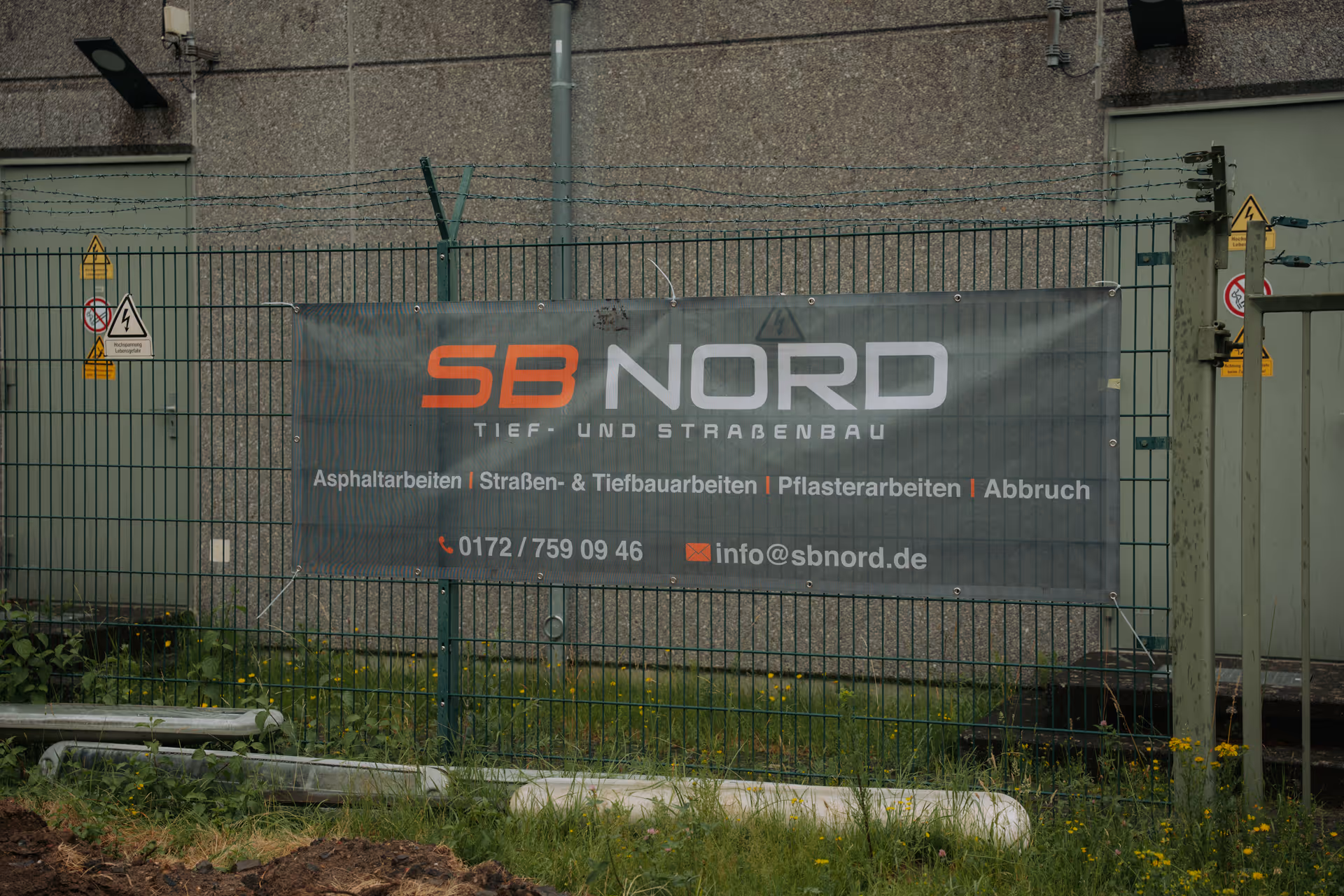 Werbebanner an einem Zaun mit dem Text SB Nord Tief- und Straßenbau und Kontaktinformationen.