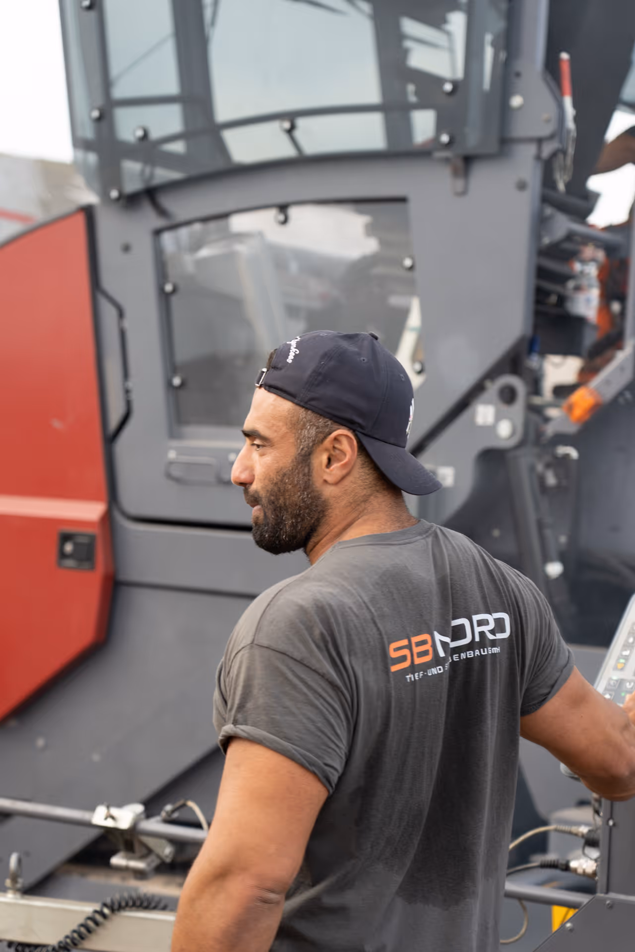 Mann mit Kappe und nassem T-Shirt an schwerer Baumaschine bedient Steuerung