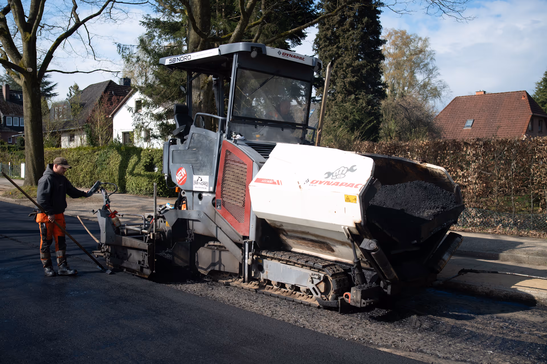 Straßenbauarbeiter bedient eine Dynapac-Asphaltmaschine zum Verlegen von frischem Asphalt auf einer Wohnstraße.