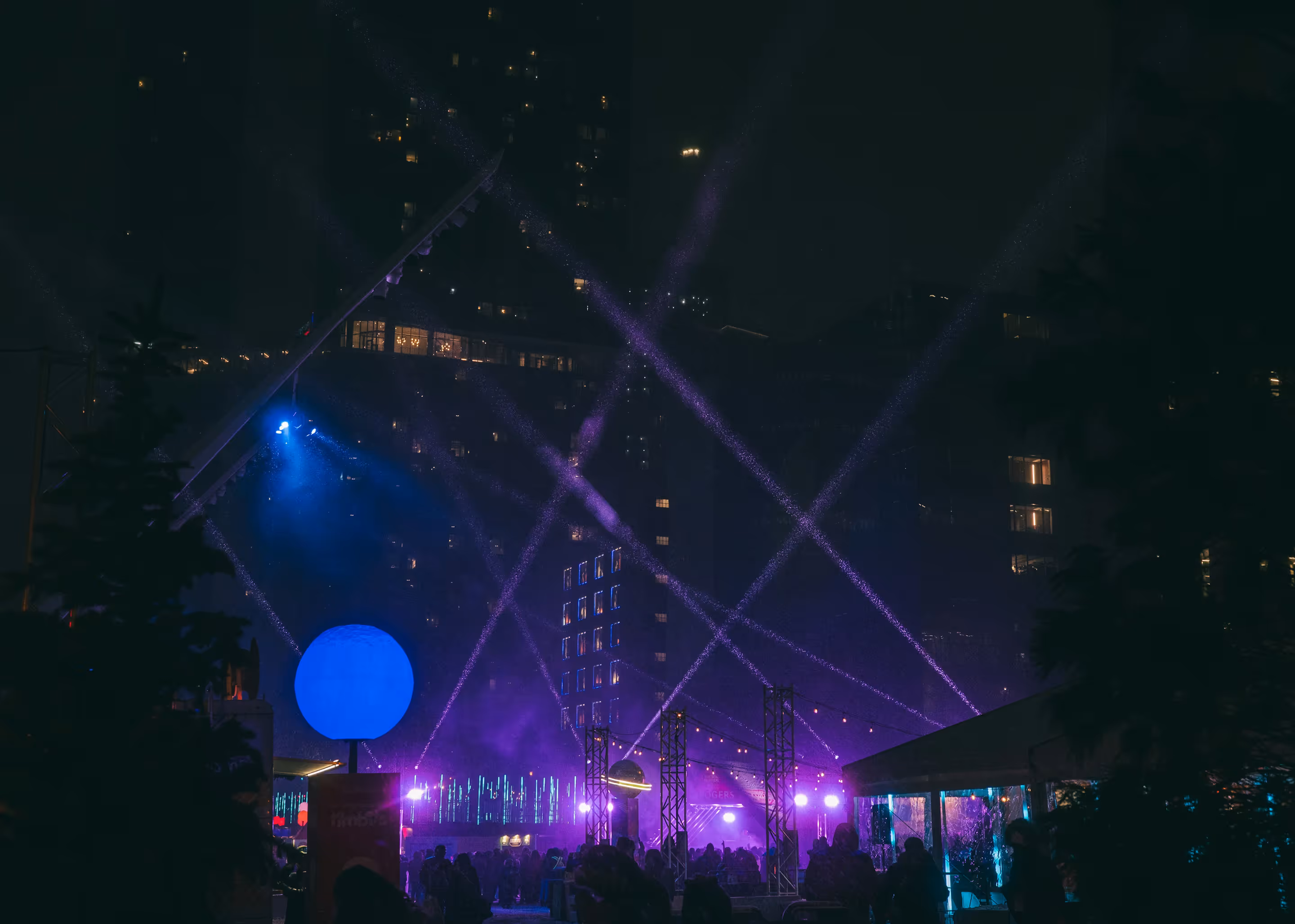 Nighttime outdoor event with purple spotlights, a large blue globe light, and silhouetted crowd.