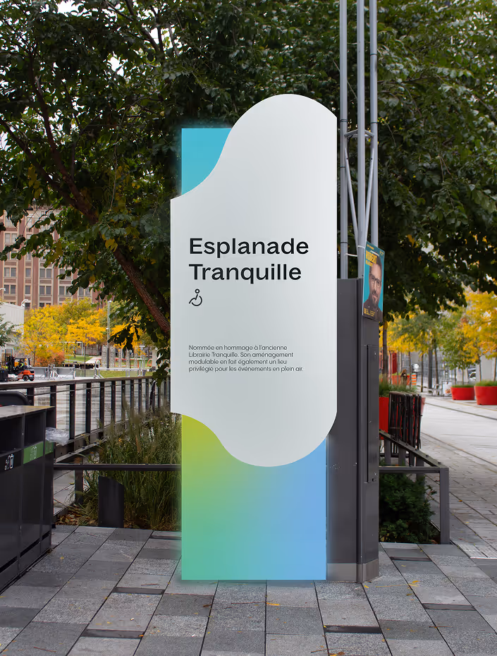 Sign for Esplanade Tranquille with a dedication in French, set outdoors near trees and a walkway.