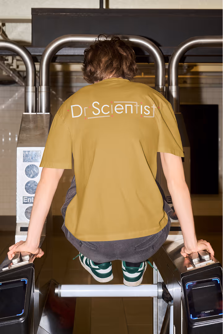Person in green sneakers and tan Dr Scientist shirt perched over subway turnstile.