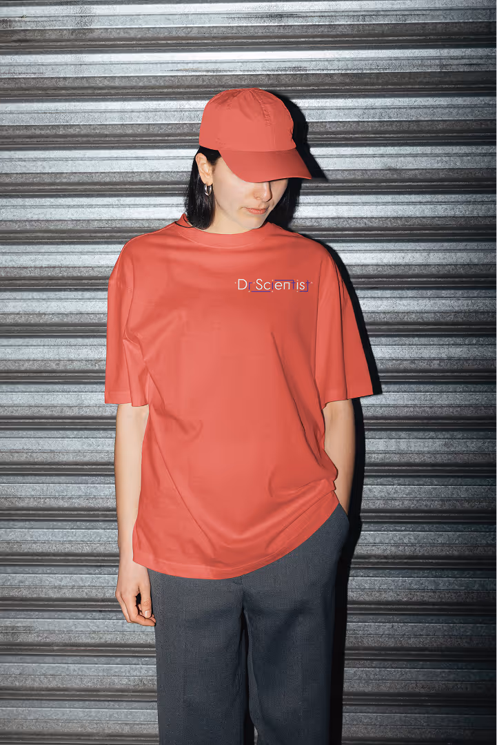 Person wearing a coral cap and t-shirt with 'Dr Scientist' text, standing against metal shutter.