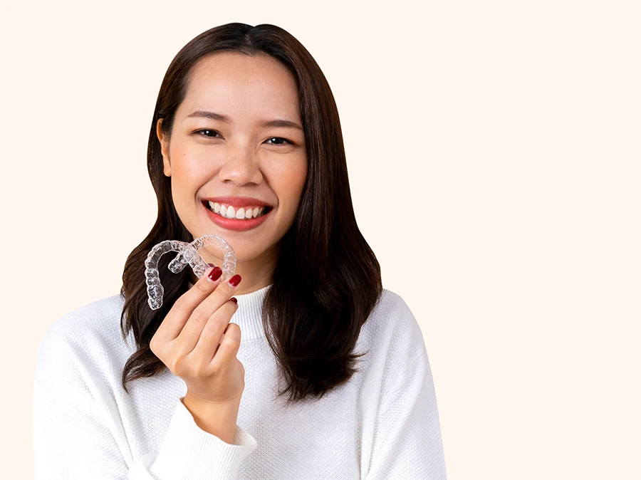 Smiling woman in white sweater holding two clear dental aligners in her hand.