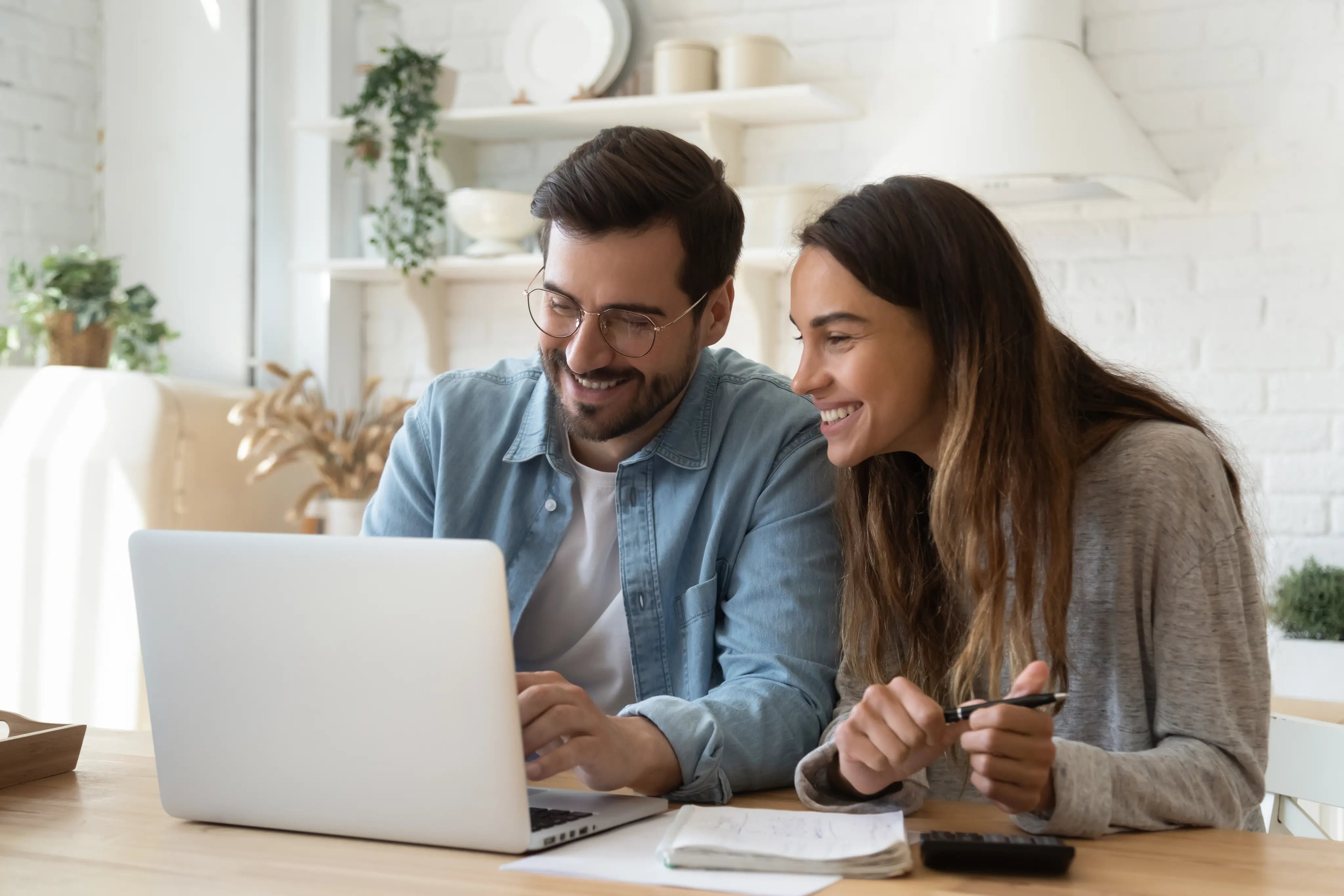 Smiling man and woman looking at laptop screen together at a wooden table with documents.