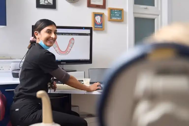 Smiling dental professional sitting at desk with a dental scan image on a computer screen.