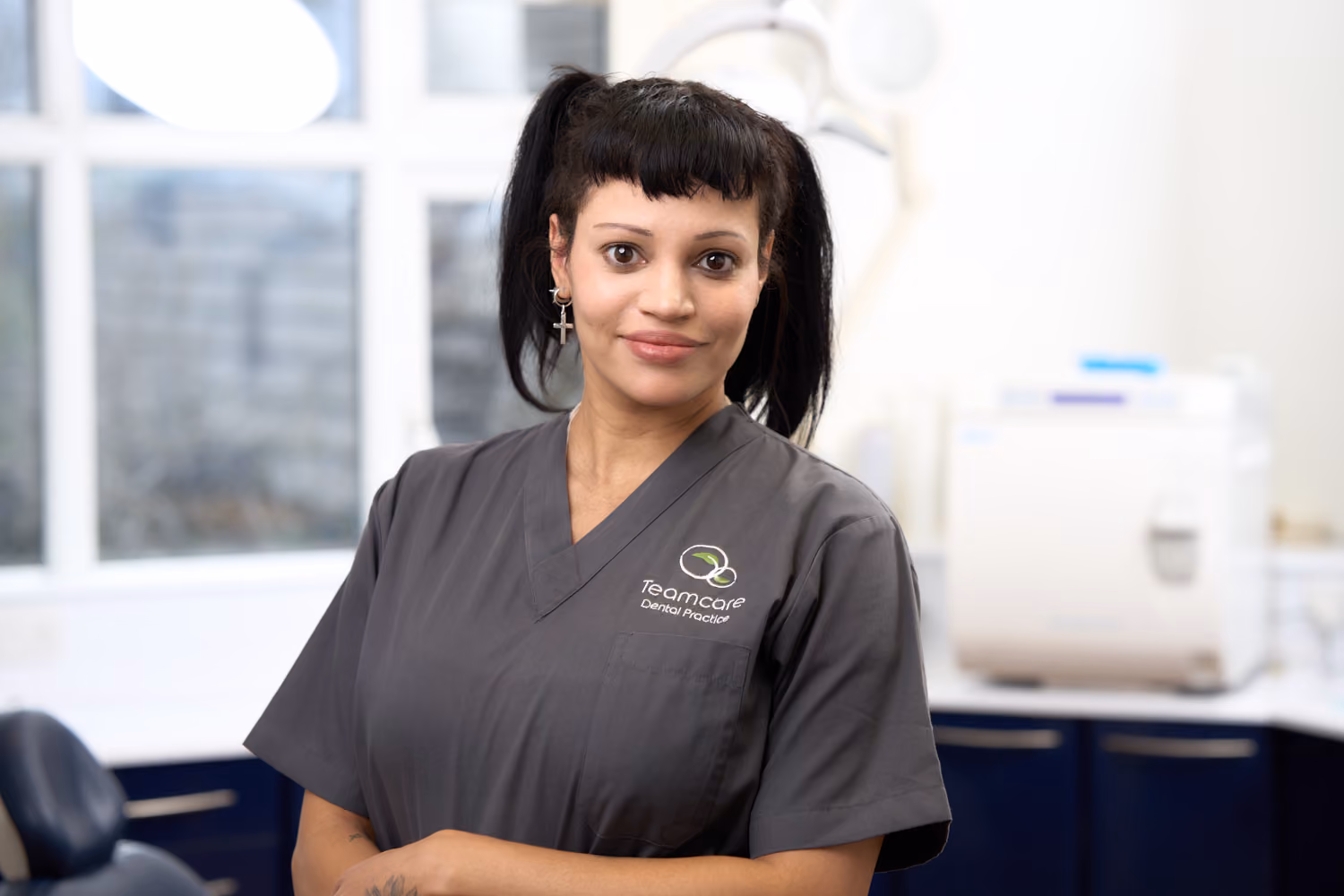 Female dental professional wearing gray scrubs with a Teamcare Dental Practice logo in a dental office.