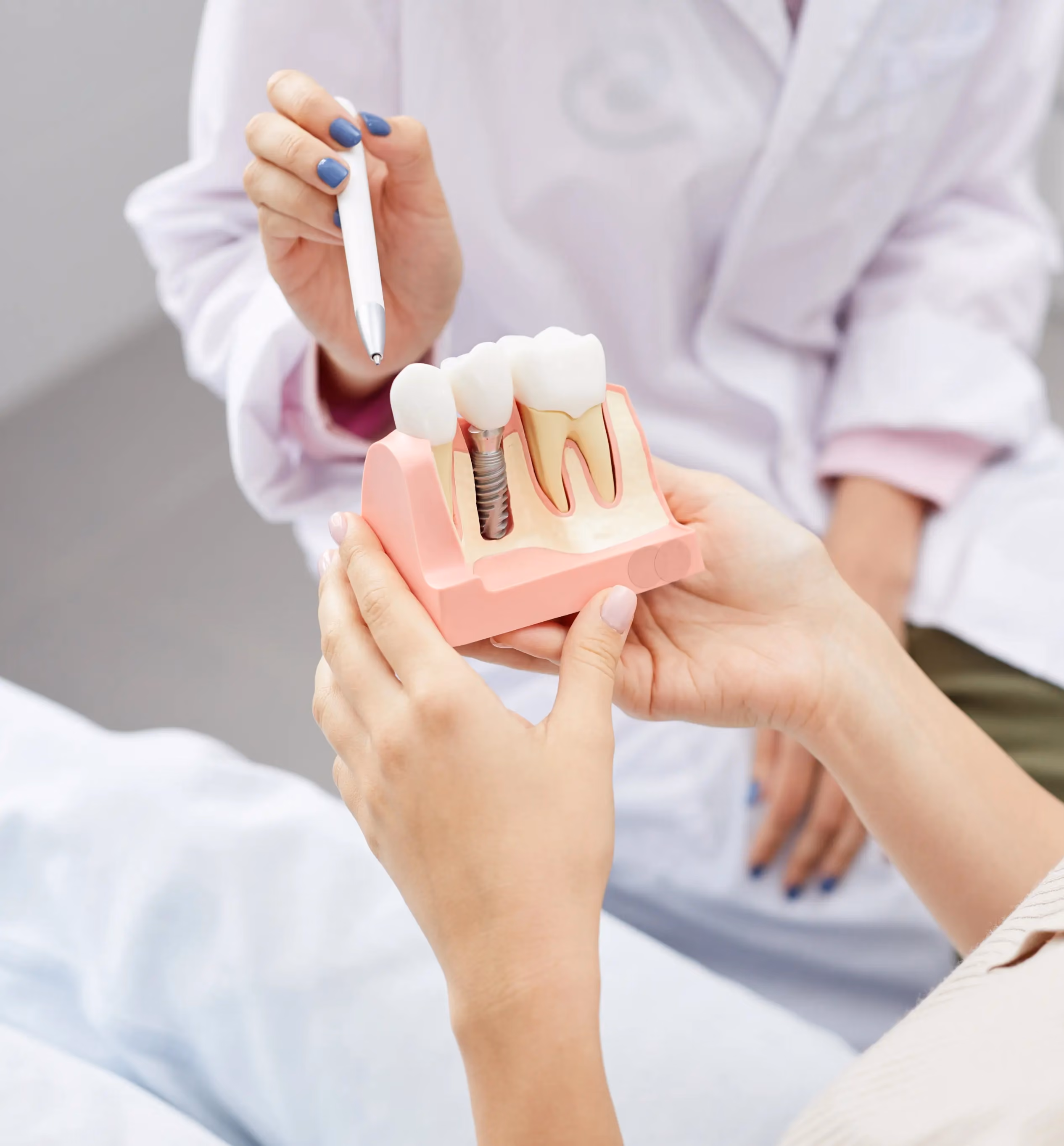 Dentist showing a dental implant model to a patient with a pen pointing to the implant.