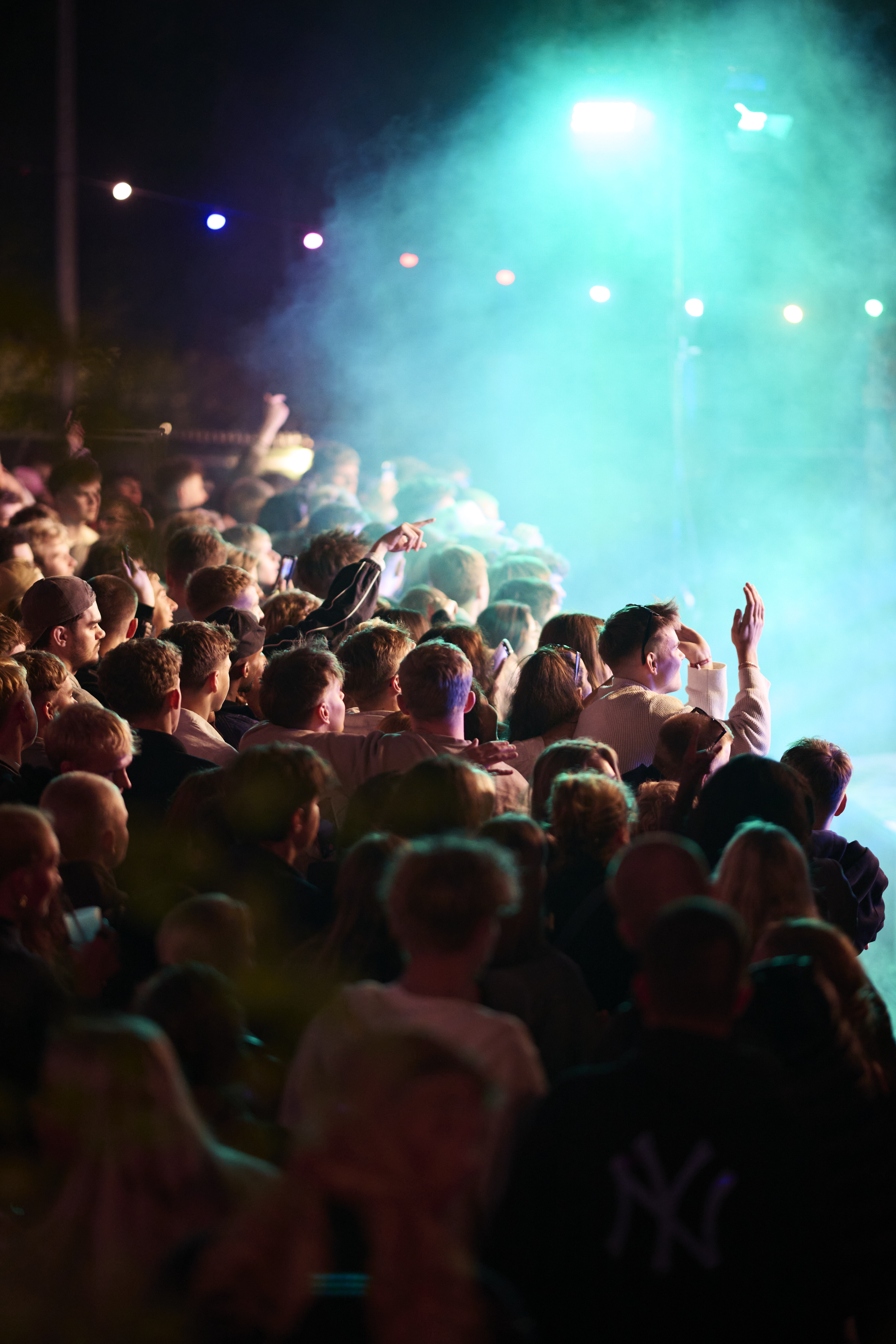 Large crowd of people at an outdoor concert with blue stage lights and smoke.