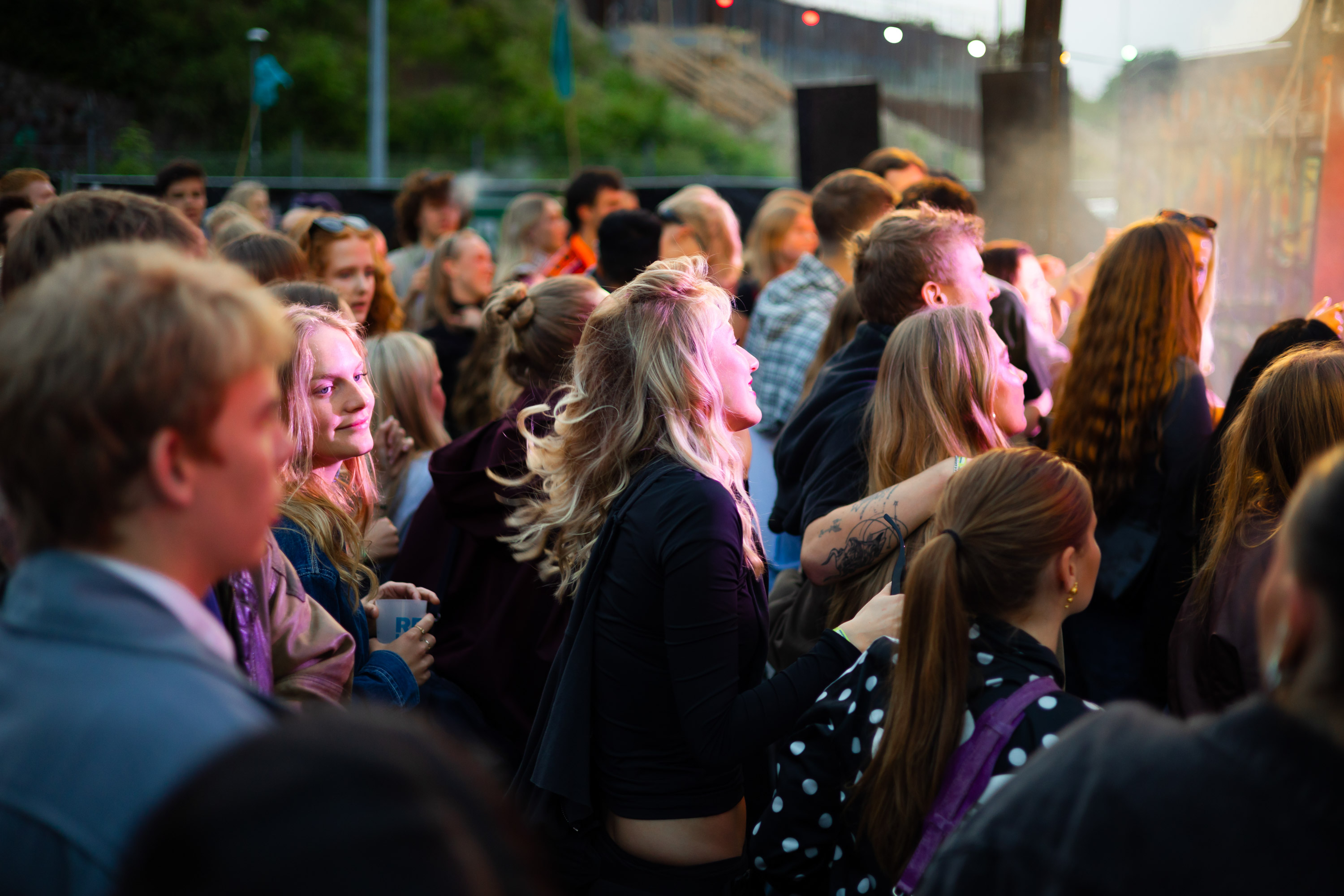 Crowd of young people enjoying an outdoor concert in the evening with colorful stage lighting.