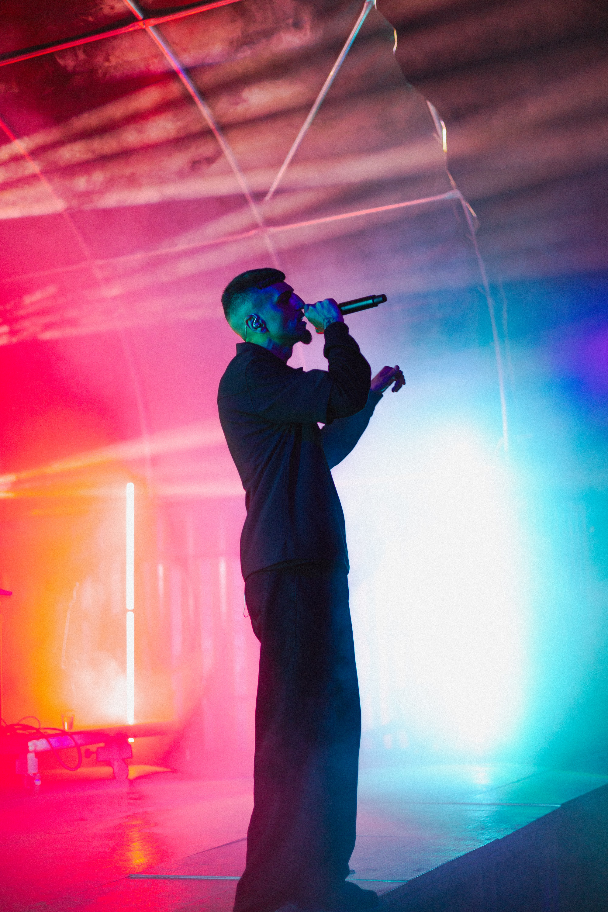 Male singer performing on stage with colorful red and blue lights and smoke effects.