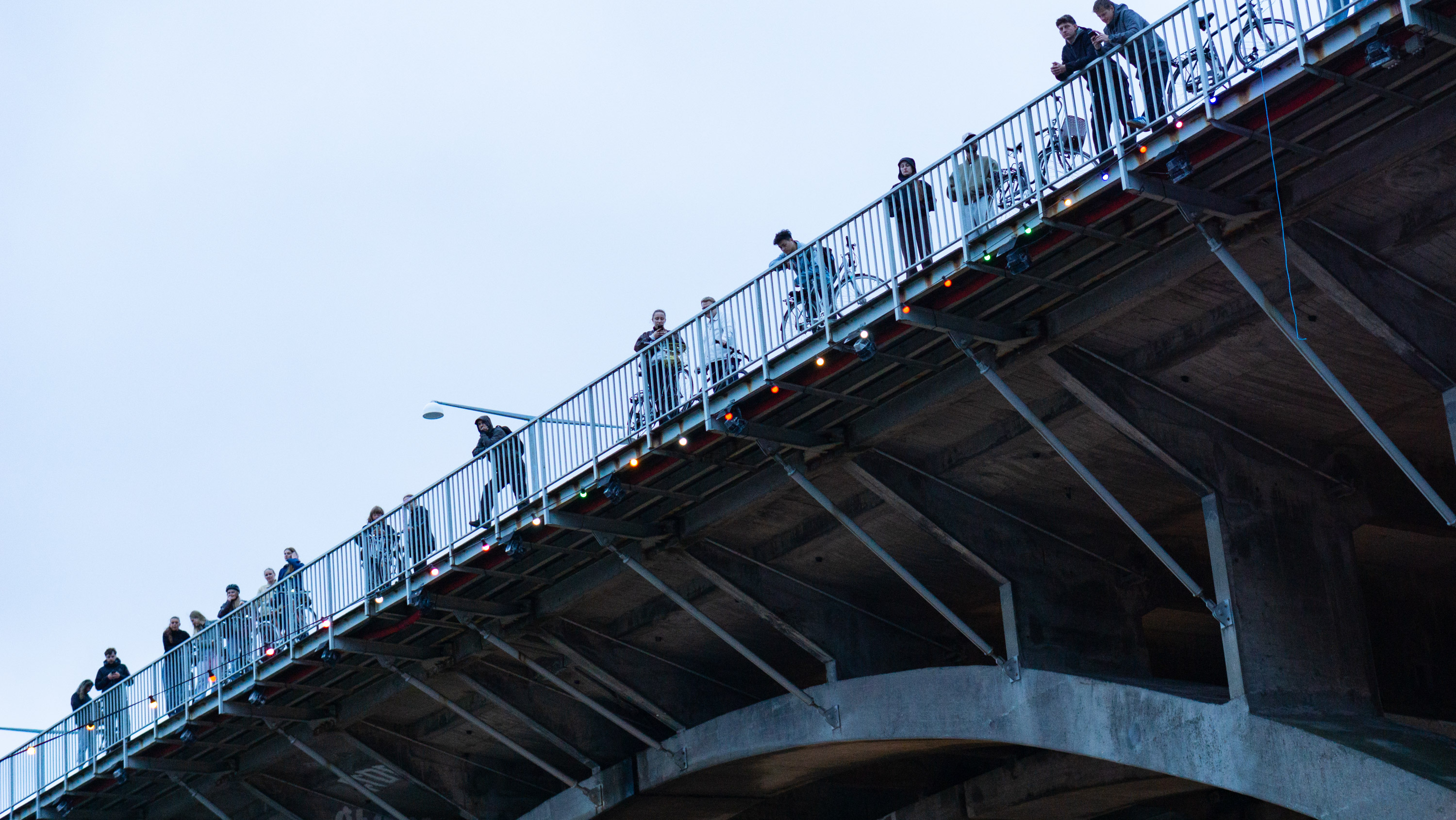 People standing and leaning on a railing of a large concrete bridge with bicycles.
