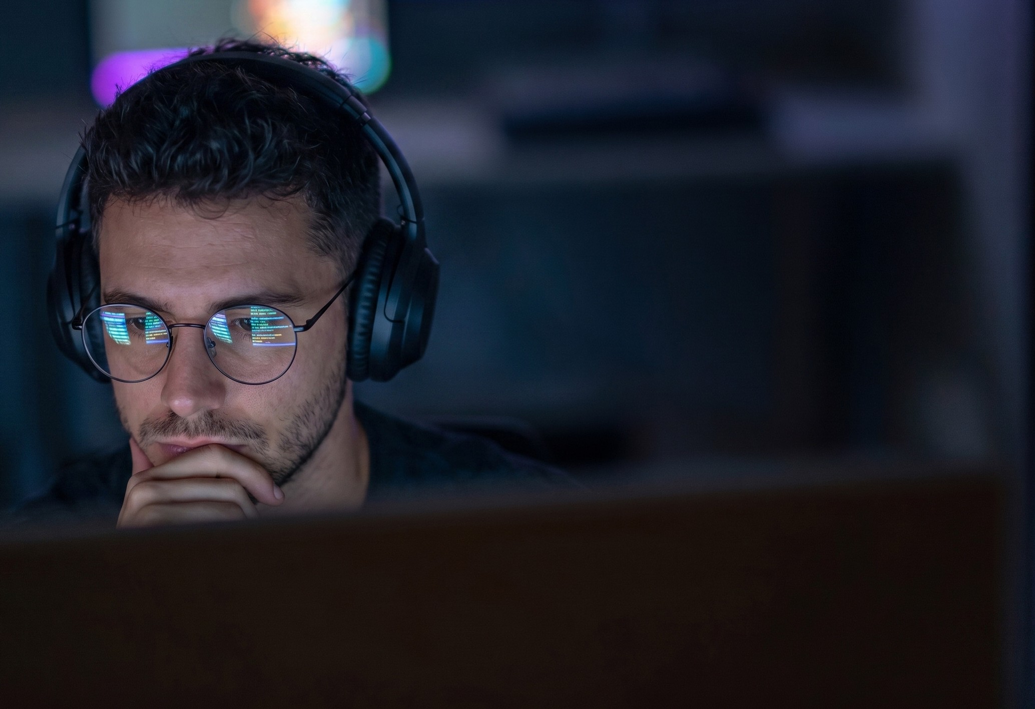 Man with glasses and headphones focused on computer screen showing code reflections.