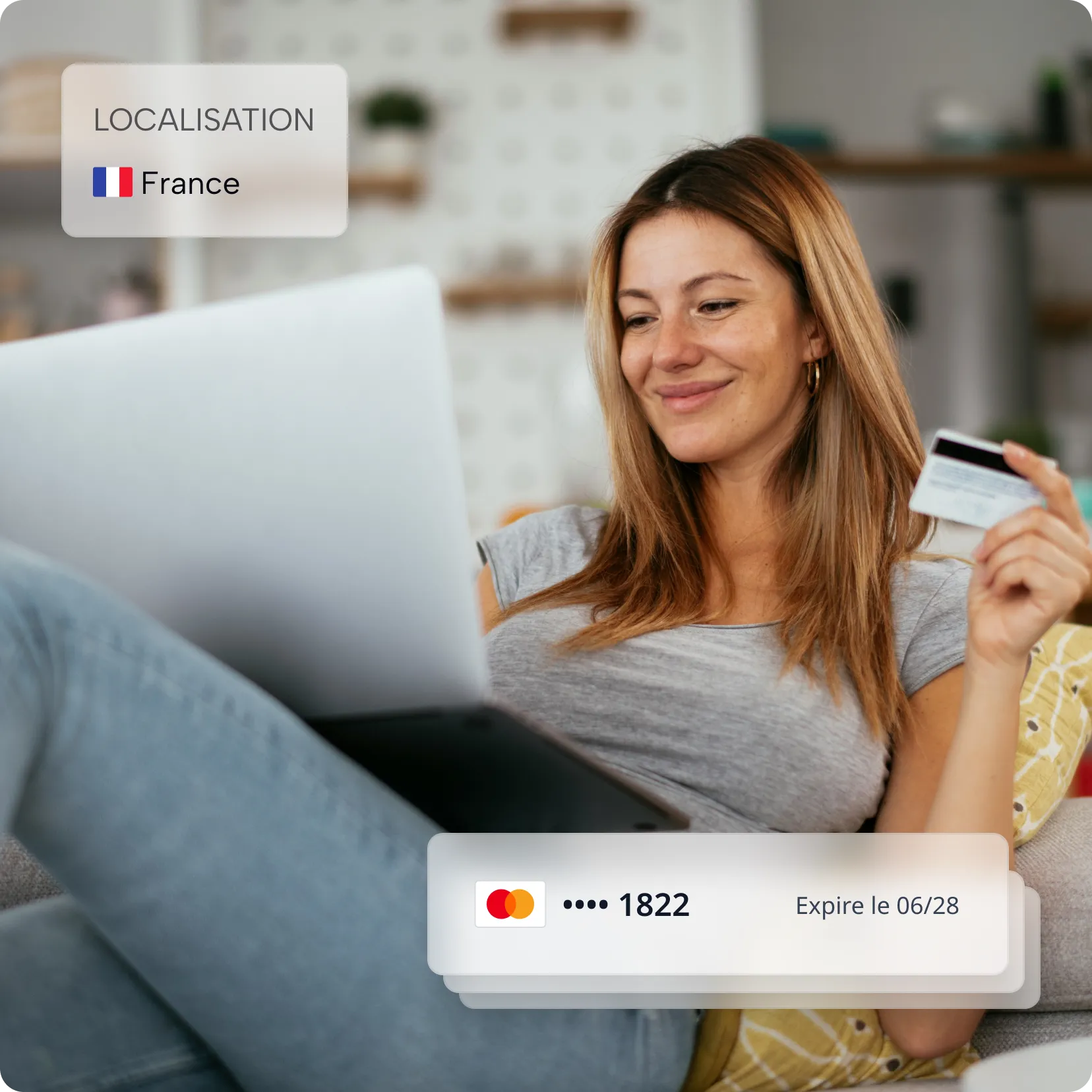 Une femme souriante tient une carte bancaire et utilise un ordinateur portable en France.