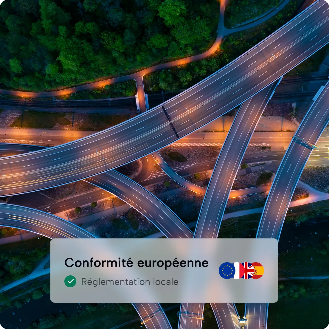 Vue aérienne d'un échangeur routier complexe éclairé la nuit près d'une zone boisée.