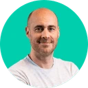 Portrait d'un homme souriant avec un t-shirt blanc sur fond turquoise.