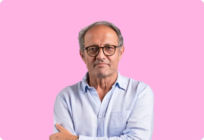Homme mûr avec lunettes et chemise bleue posant devant un fond rose uni.