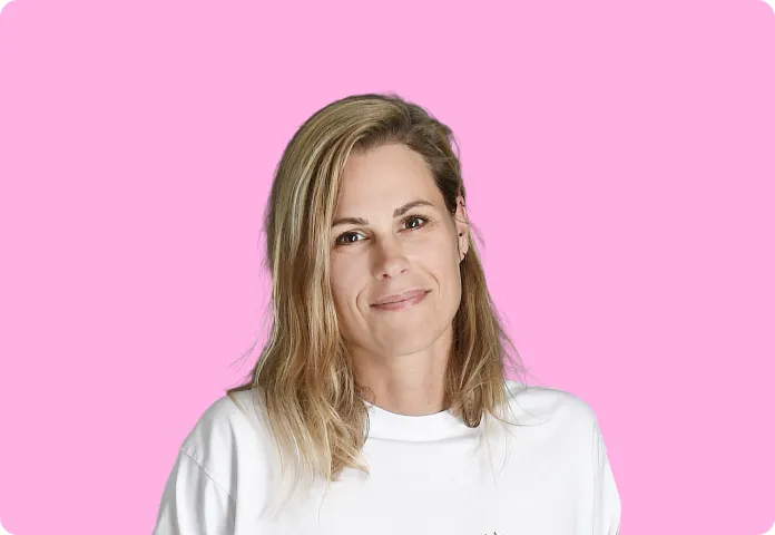 Femme souriante aux cheveux blonds portant un t-shirt blanc sur fond rose.