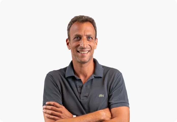 Homme souriant avec un polo gris foncé, les bras croisés, sur fond blanc.