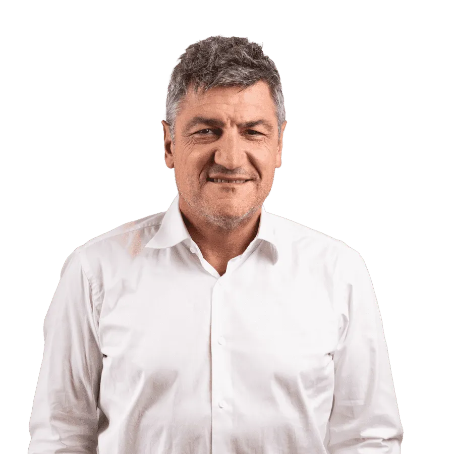 Homme mûr avec cheveux gris et chemise blanche souriant légèrement devant un fond transparent.