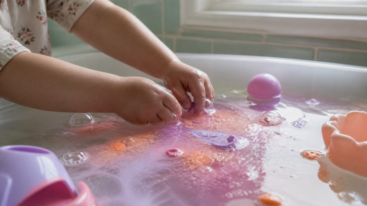 Toddler playing with colored water tablets in bath