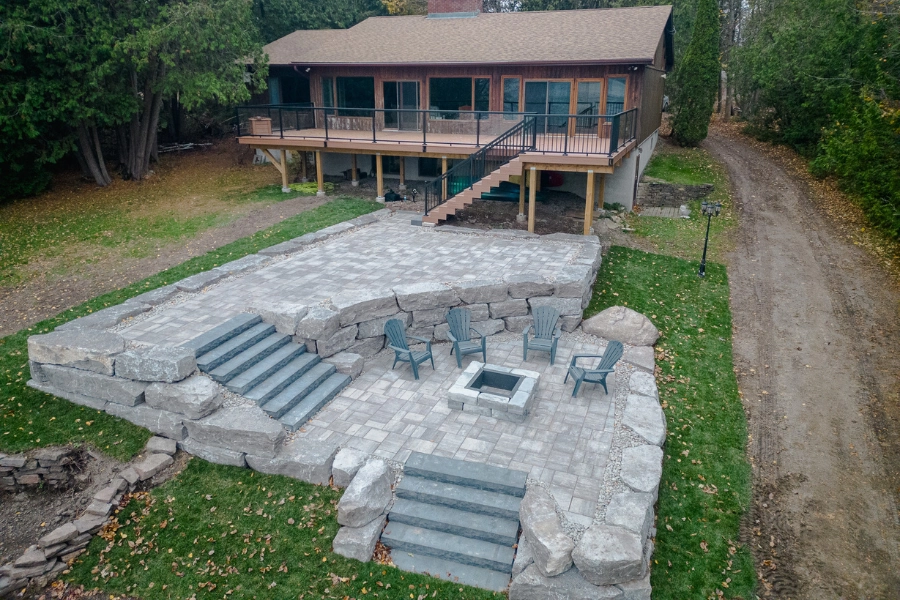 Natural stone patio with fire pit and built-in steps at a Kawartha Lakes cottage backyard by TEG Contracting