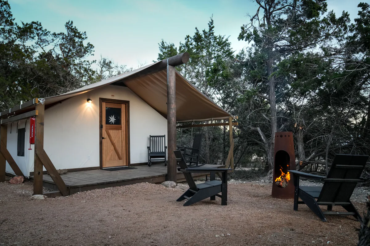 A safari tent at Lucky Arrow Springs at dusk, chiminea lit beside Adirondack chairs