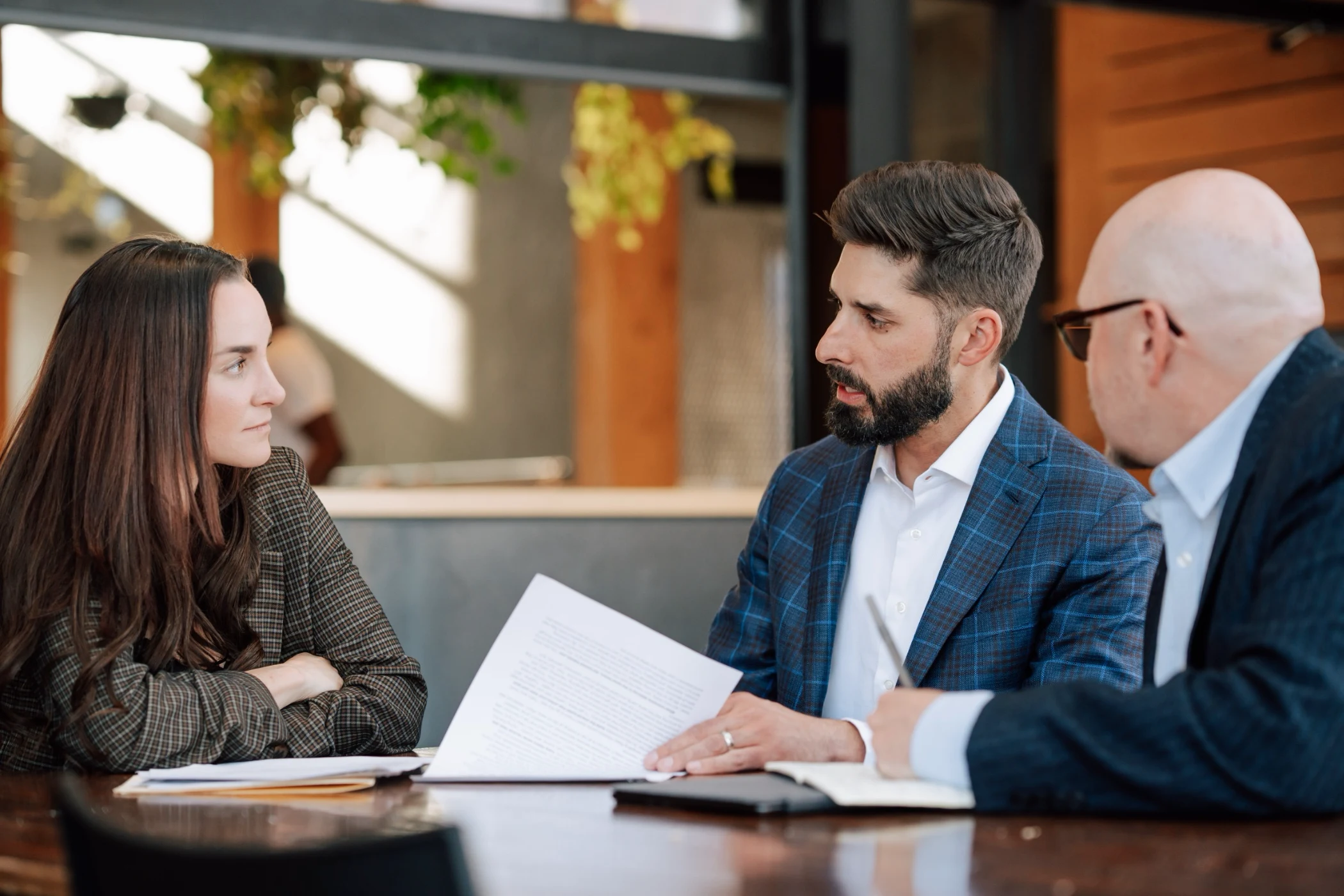 Three business professionals having a serious discussion at a table with documents in a modern office.