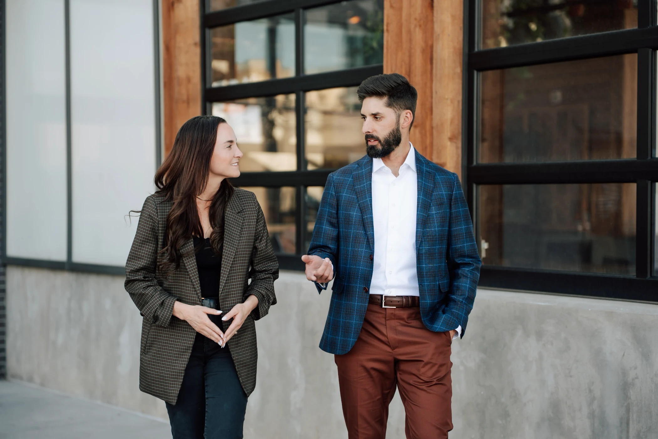 Man and woman walking and talking outside a building with large windows.