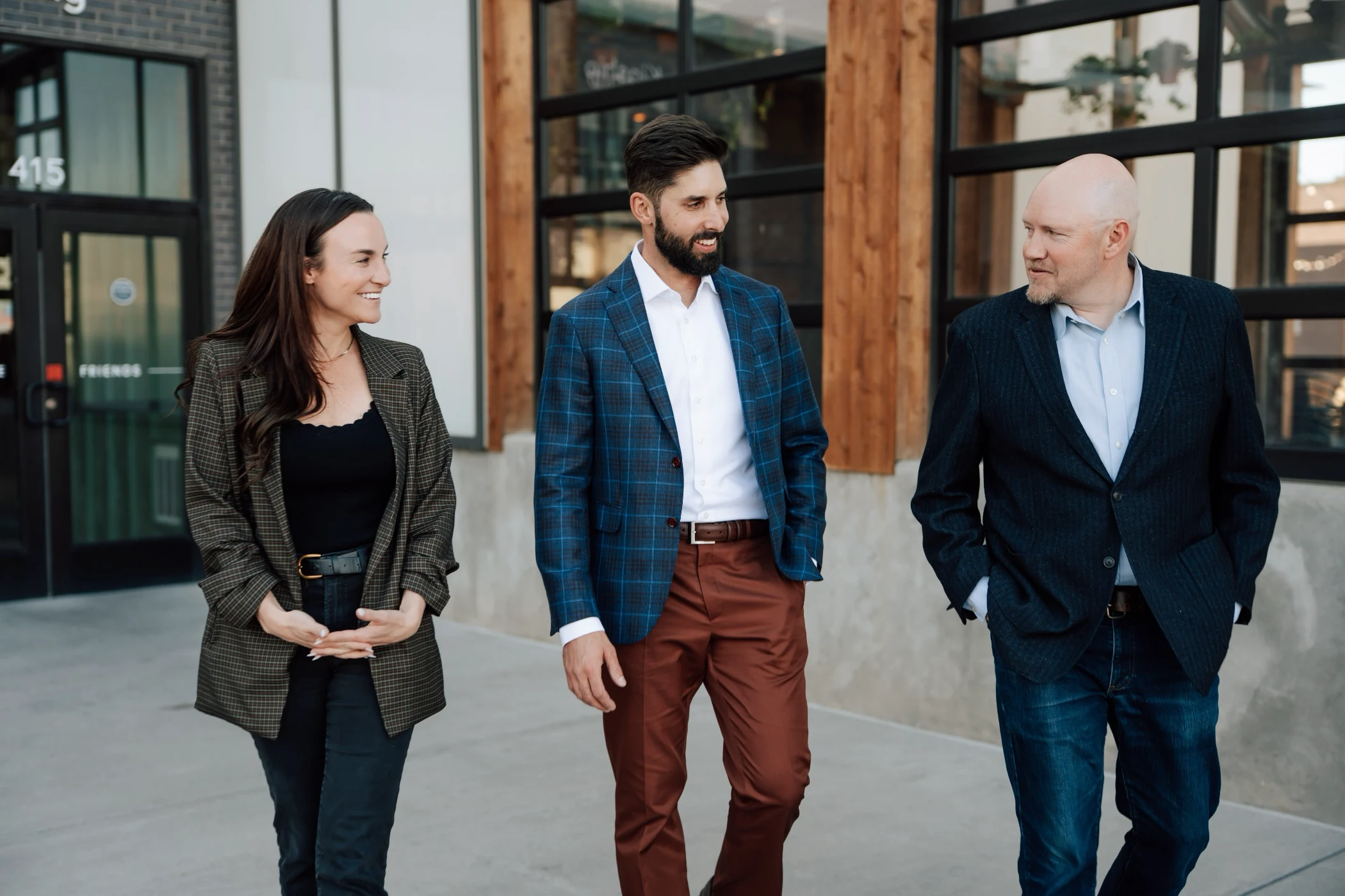 Three professionally dressed people walking and conversing outside a modern building.