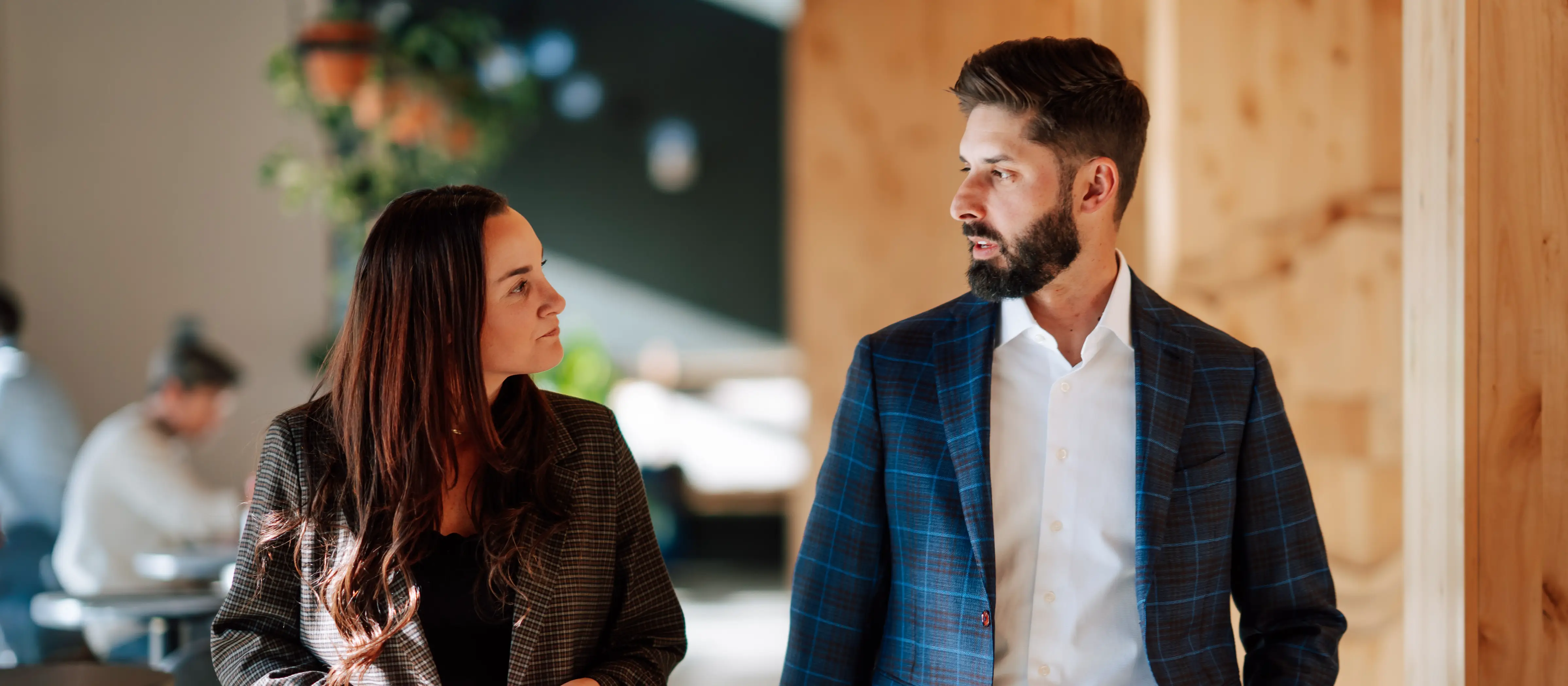 Two professionally dressed people, a woman and a man, engaged in conversation while walking indoors.