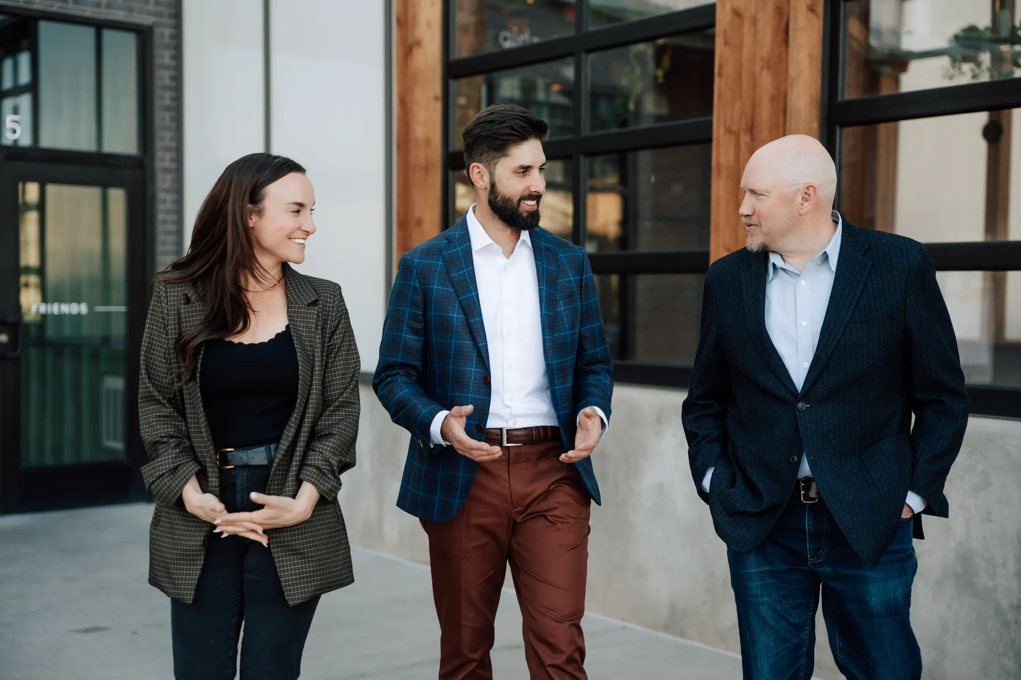 Three colleagues in business casual wear smiling and walking outside a modern building.