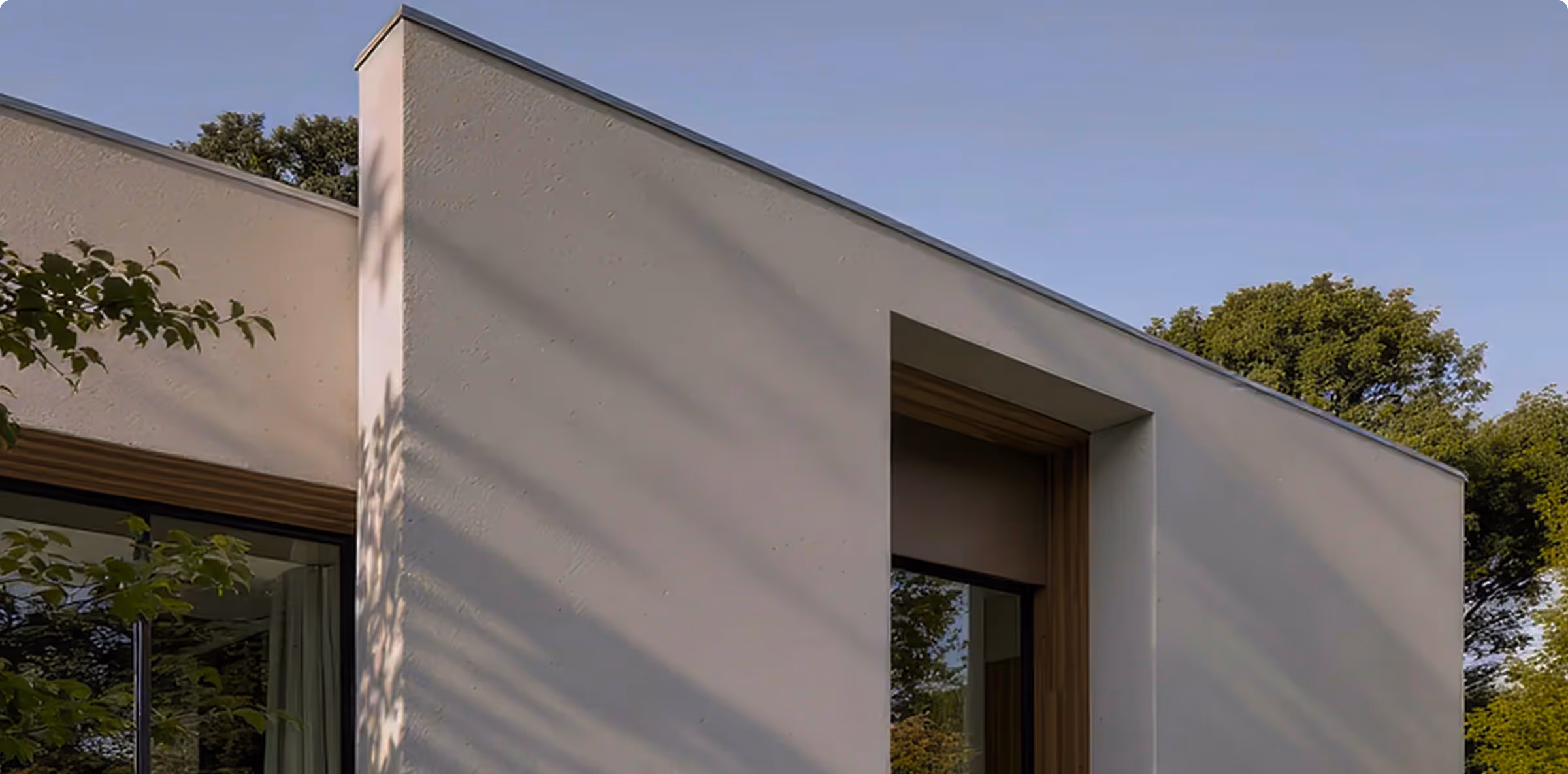 White modern house facade with large window and trees reflected in glass under clear blue sky.