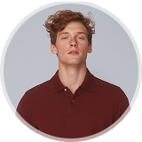 Young man with wavy brown hair wearing a maroon polo shirt against a gray background.