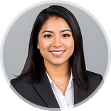 Professional woman with long dark hair wearing a black blazer and white shirt, smiling against a gray background.