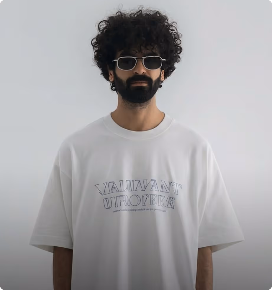 Man with curly hair and beard wearing sunglasses and a white t-shirt with printed text.