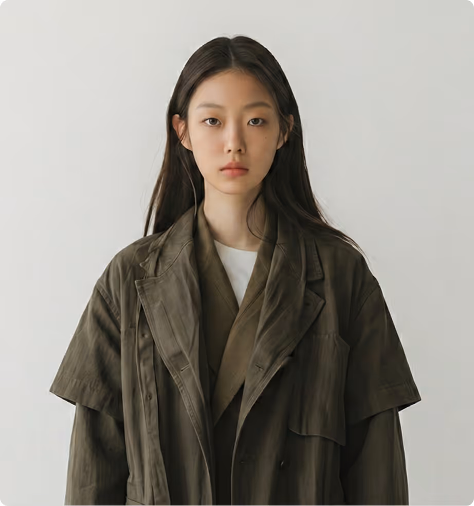 Young woman with long dark hair wearing layered dark olive jackets against a plain light background.
