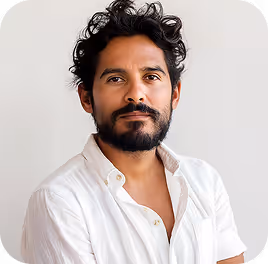 Man with dark curly hair and beard wearing a white shirt against a plain background.