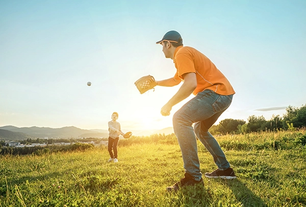 An action shot of the same father and son playing catch on the homepage. The father is poised and ready to catch his son's fastball. It is a beautiful day.