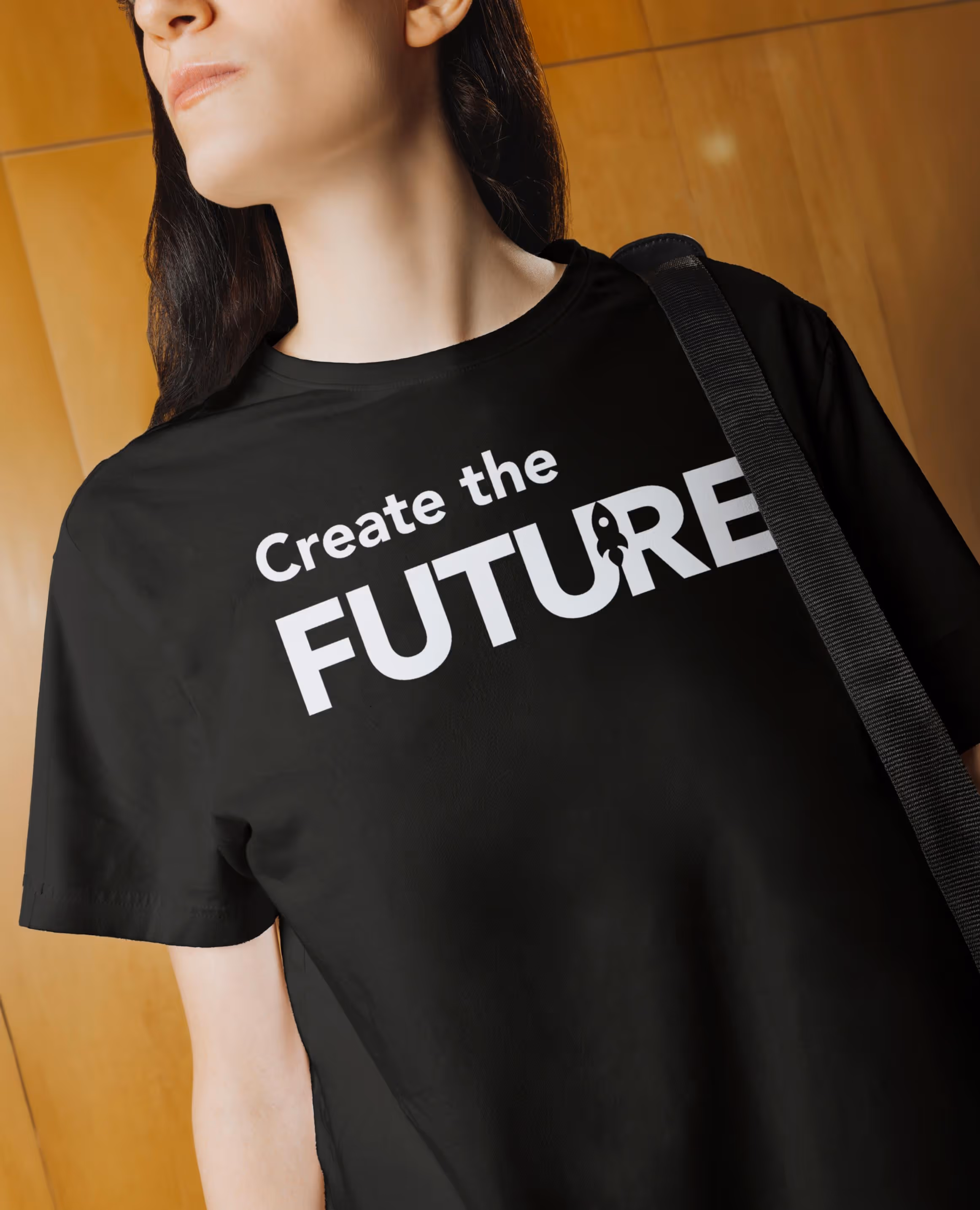 A person wearing a black t-shirt printed with "Create the FUTURE" in white type, a bag strap across one shoulder.