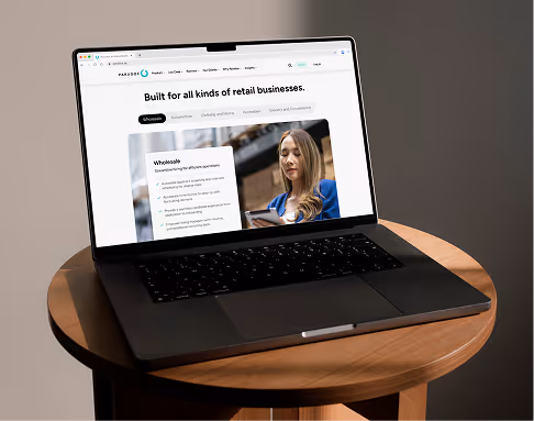 A laptop on a round wooden table displaying a Paradox web page headlined "Built for all kinds of retail businesses."